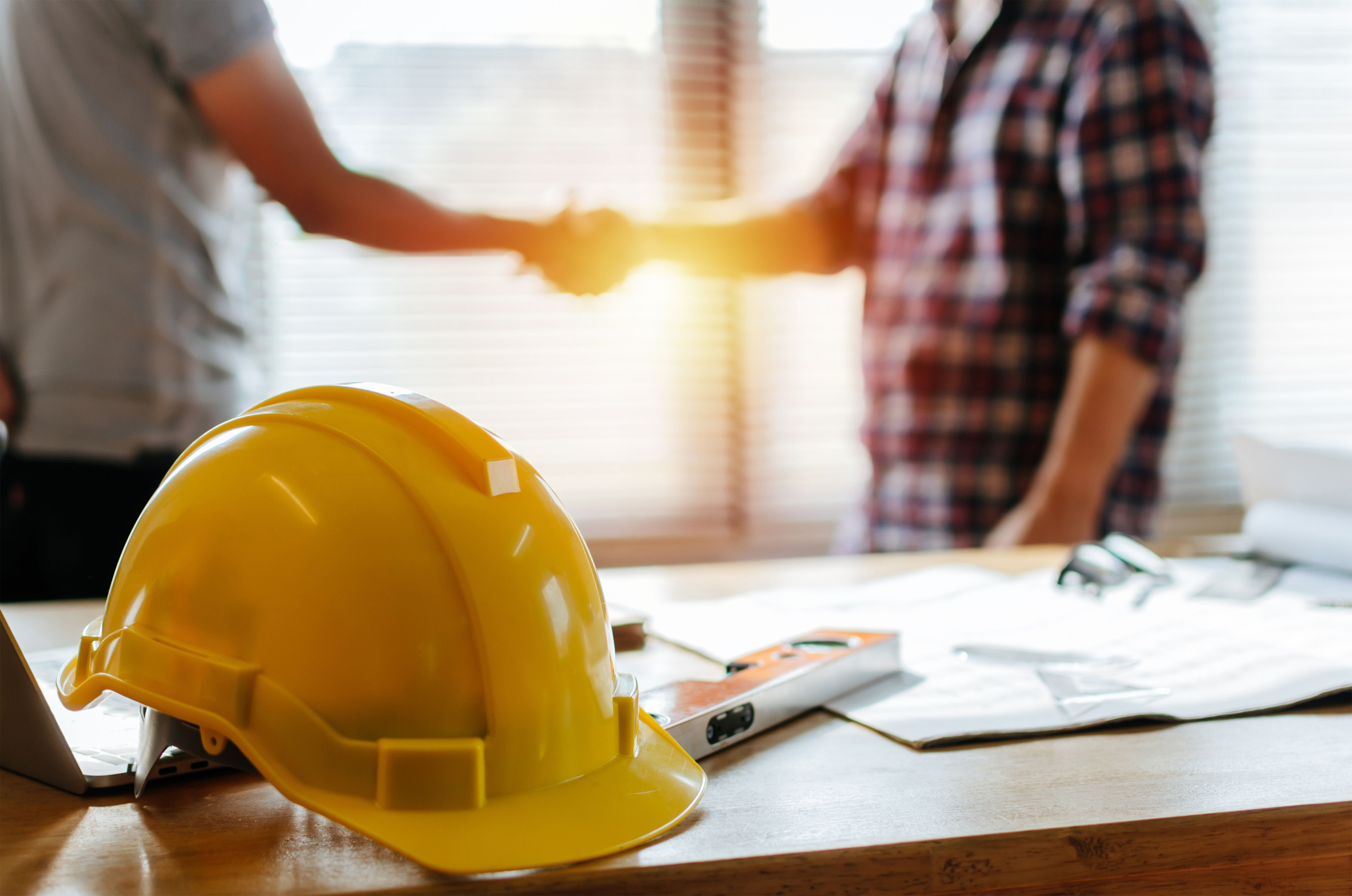 Yellow hard hat on table with construction team shaking hands in background